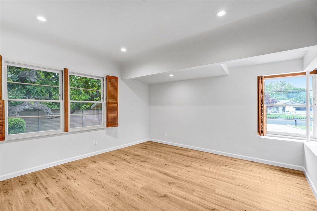 A room with wooden floors and white walls, with windows showing a view of a fence and trees.