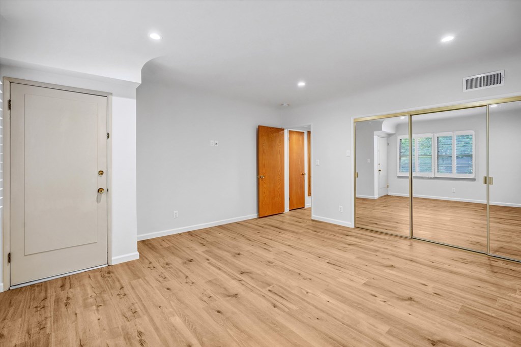 A room with wooden floors and white walls, with a door on the left and a glass door on the right.