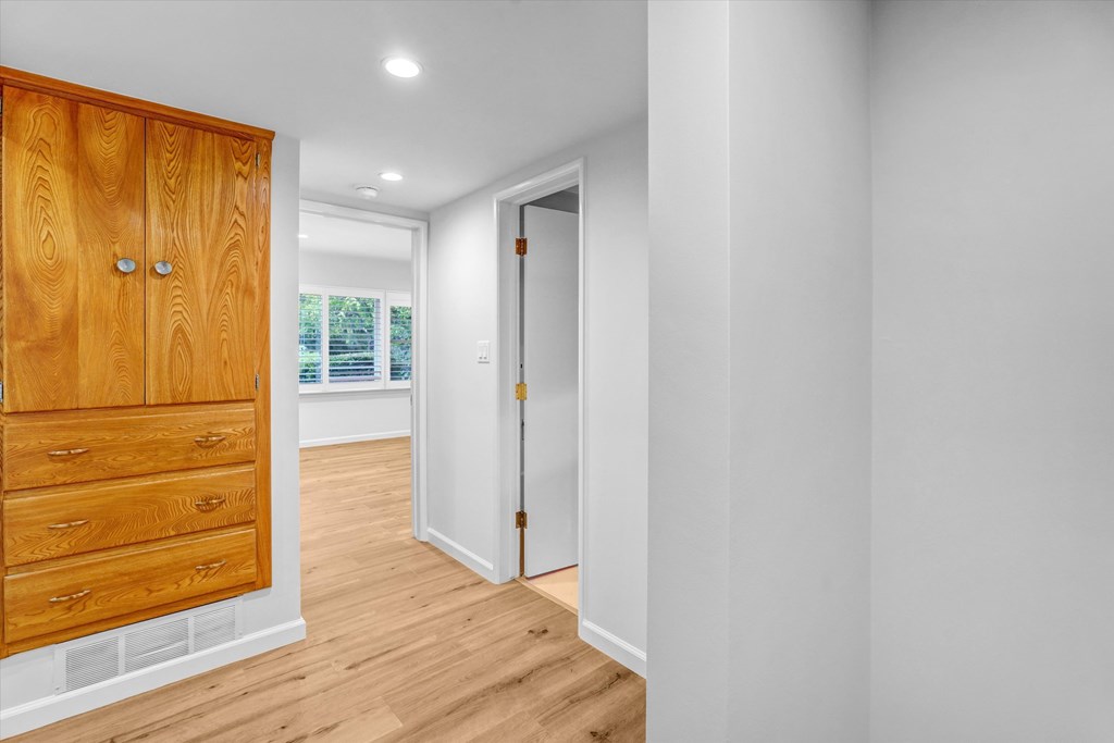A white hallway with a wooden cabinet and a door.