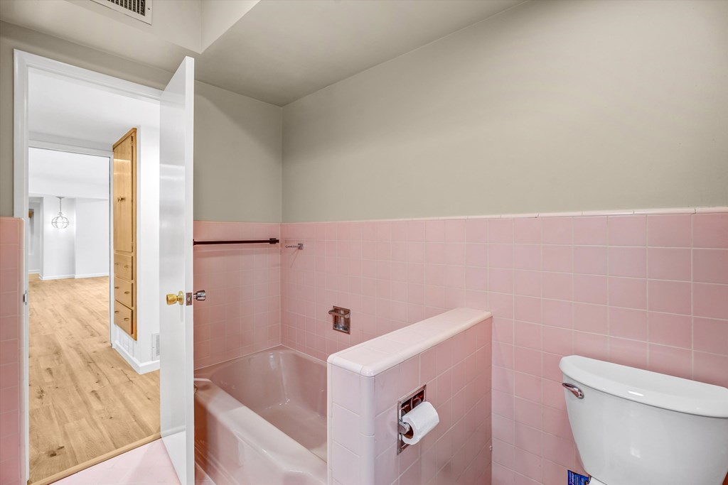 A bathroom with a pink wall and a white tub.