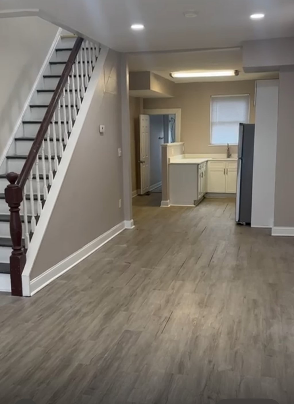 A kitchen with a refrigerator, cabinets, and a staircase.