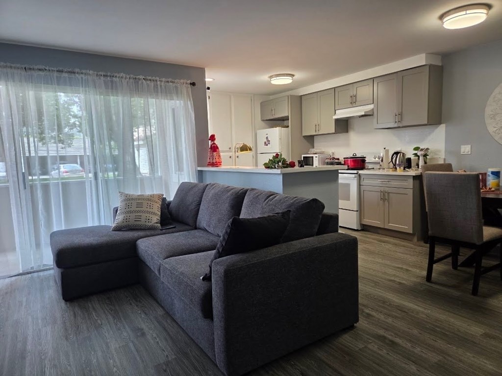 A grey couch with a grey pillow is in front of a kitchen.