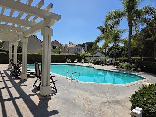A pool surrounded by a white pergola and palm trees.