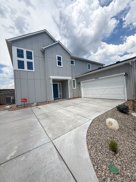 A grey house with a white garage door and a red sign on the fence.