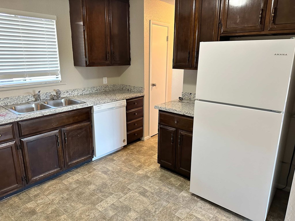 A white refrigerator stands in a kitchen with dark wood cabinets.