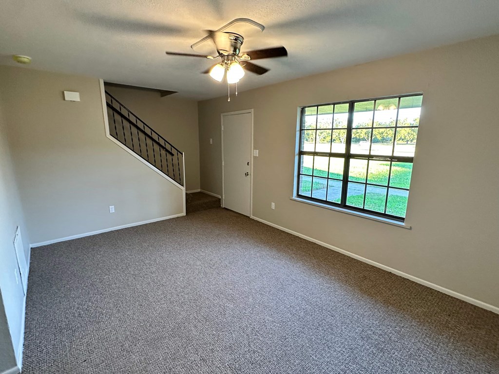 A room with a carpeted floor, a ceiling fan, and a window with a view of a lawn.