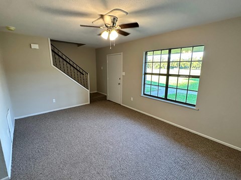 A room with a carpeted floor, a ceiling fan, and a window with a view of a lawn.