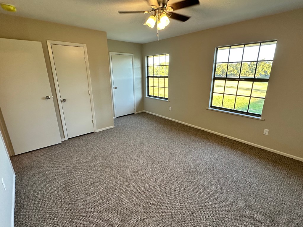 A room with a ceiling fan and two windows.