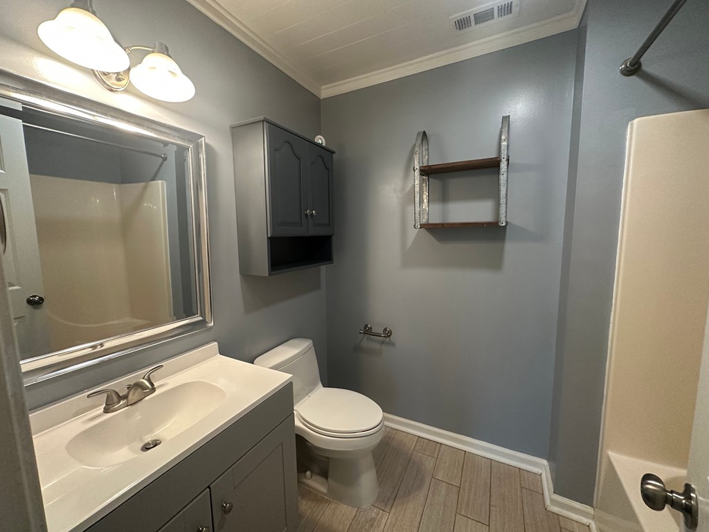 A bathroom with a toilet, sink, mirror, and shelves.