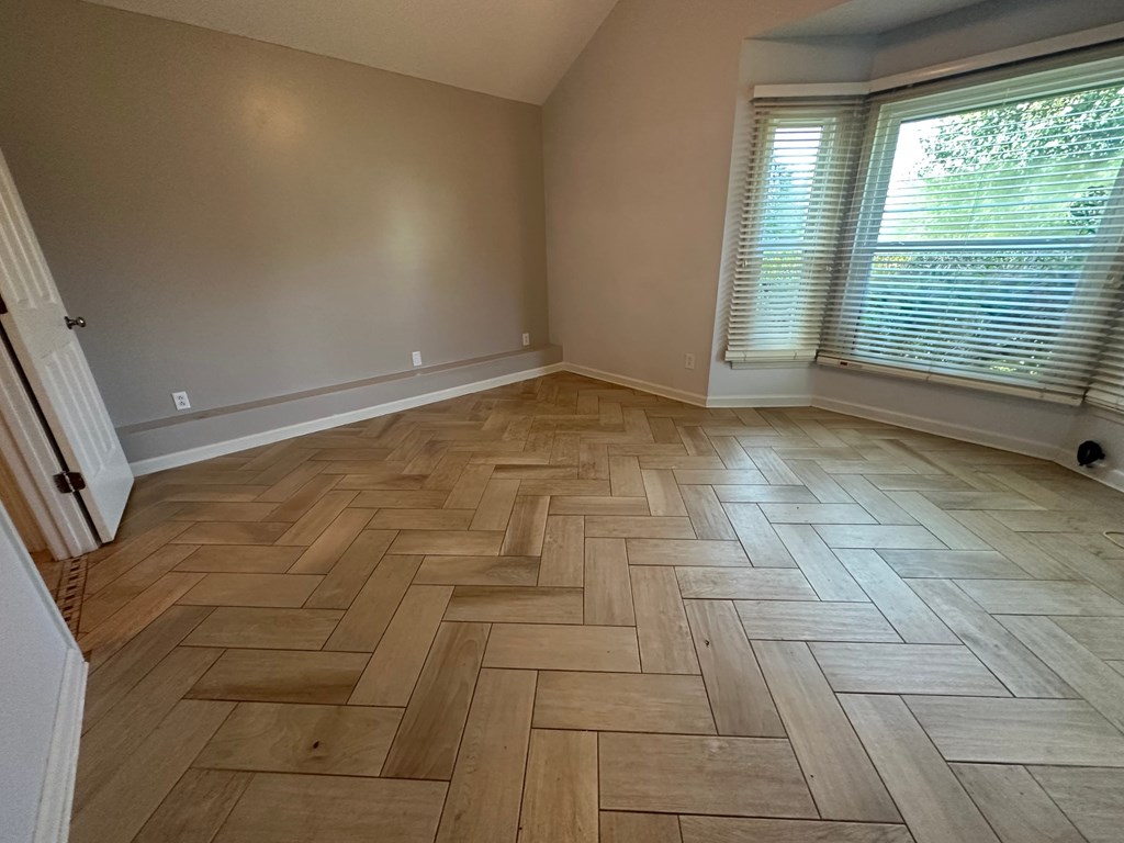 A room with wooden flooring and a window with blinds.
