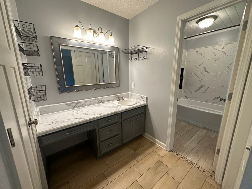 A bathroom with a marble countertop and a mirror above it.