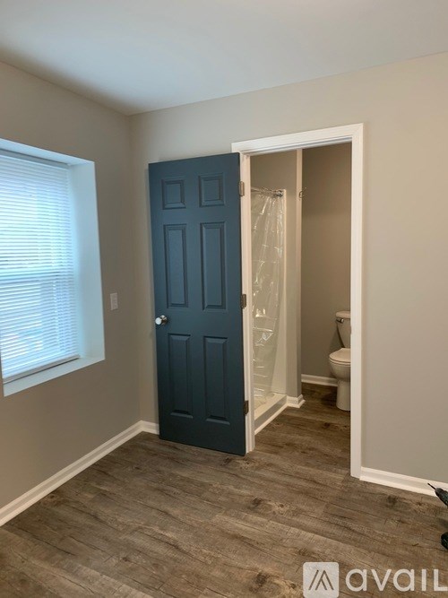 A room with a dark blue door and a toilet in the background.