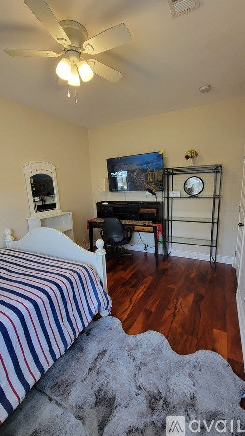 A bedroom with a bed, a chair, a desk, and a ceiling fan.