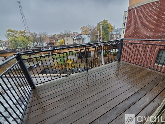 A wooden deck with a metal railing and a brick building in the background.