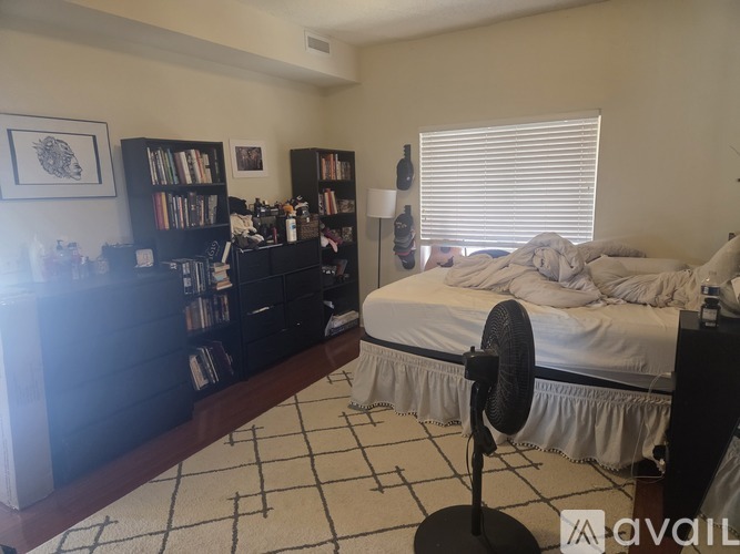 A bedroom with a bed, a fan, and a bookshelf.
