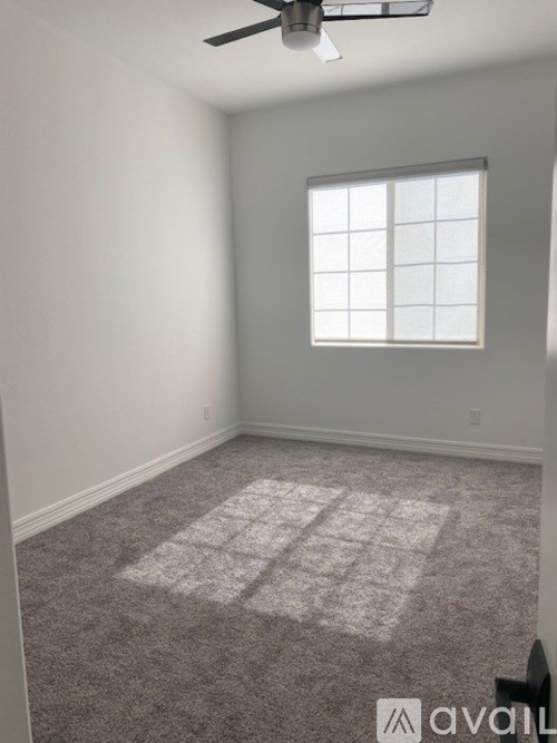 A room with a carpet, a window, and a ceiling fan.