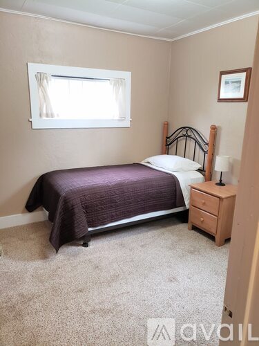 A bedroom with a bed, nightstand, and window.