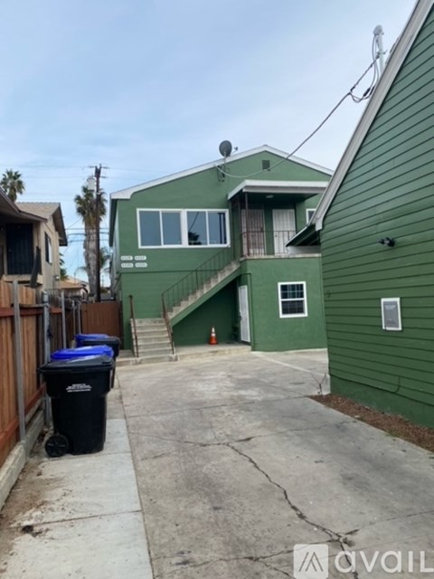 A green house with a blue trash bin in front.
