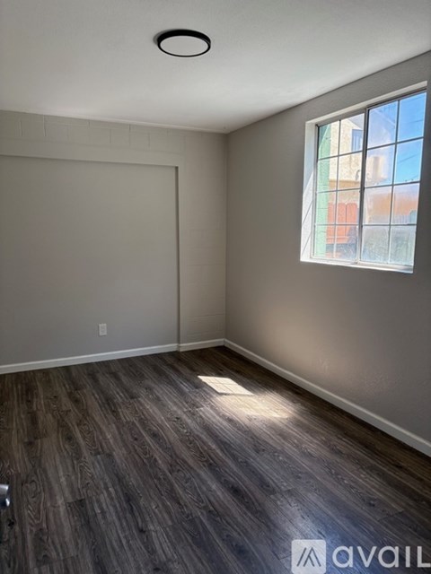 A room with wooden flooring and a window showing a view of buildings outside.