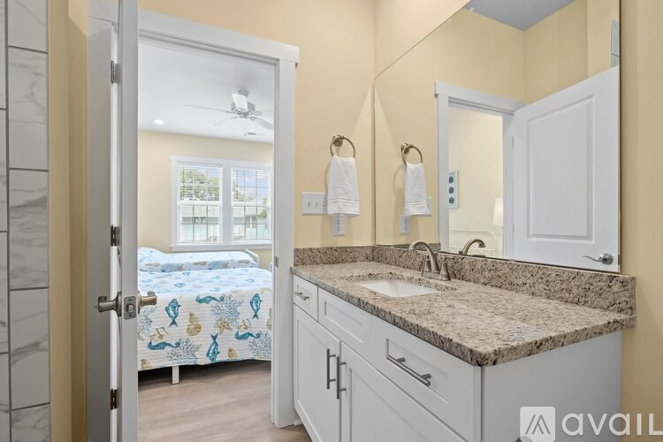 A bathroom with a marble countertop and a bedroom with a window in the background.