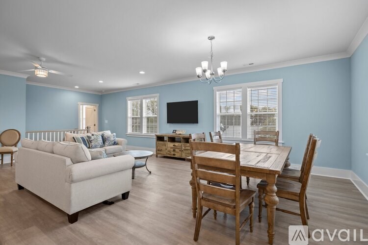 A living room with a white couch, wooden chairs, and a television.