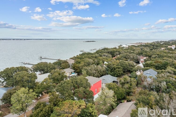 A bird's eye view of a residential area with houses surrounded by trees and a body of water in the distance.