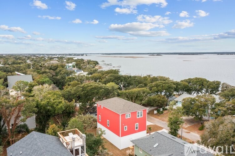 A red house is in the foreground of a scenic view with trees and a body of water in the background.