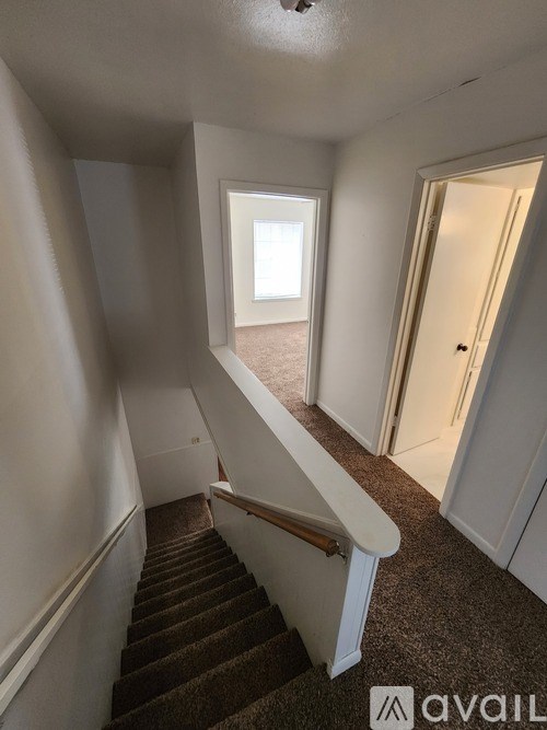 A staircase with a carpeted runner and white handrails leads to a bright room with a window.