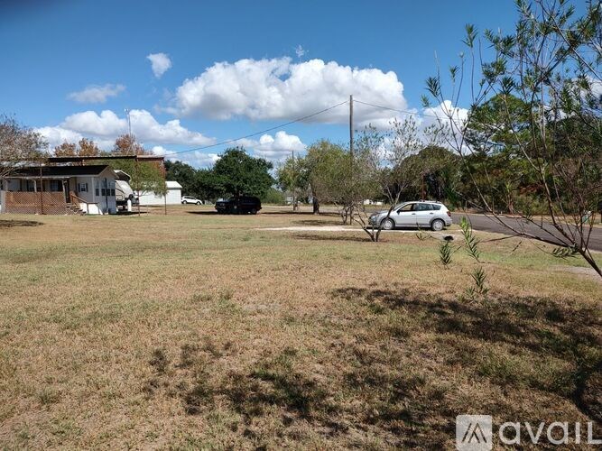 A car is parked in a grassy field with a house and trees in the background.