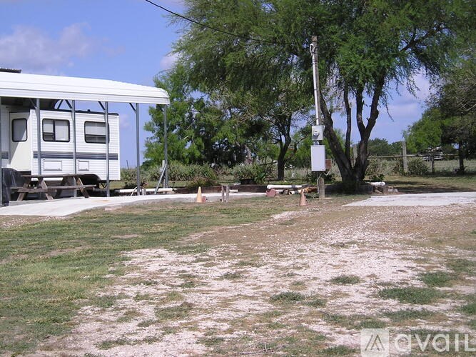 A white RV is parked in a grassy area with a picnic table and a tree.