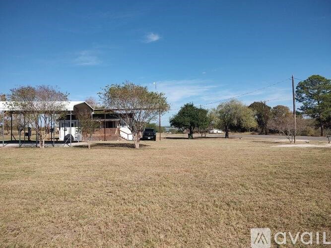 A grassy field with a building and trees in the background.