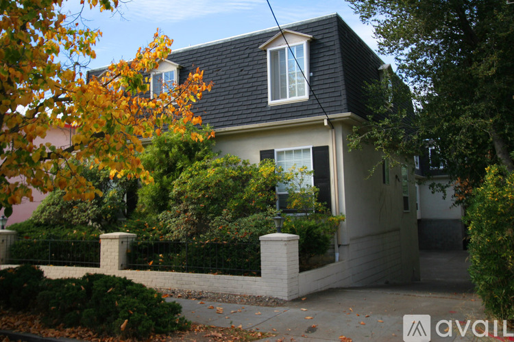 A house with a black roof and white trim is surrounded by trees and bushes.