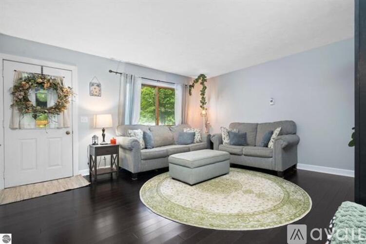 A living room with a grey couch, a green rug, and a white door.