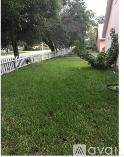 A grassy area with a white fence and trees.