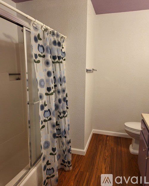 A bathroom with a toilet and a shower with a floral shower curtain.