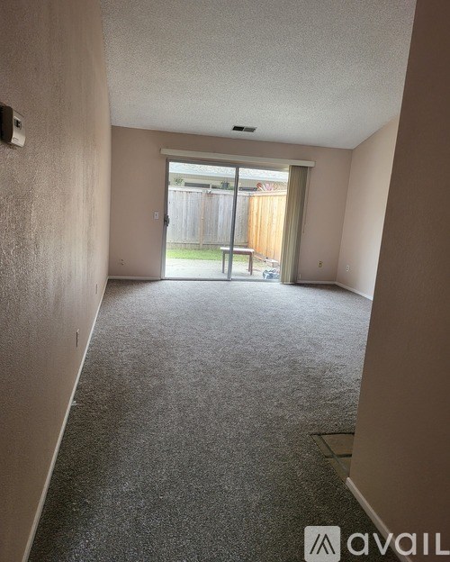 A room with a carpeted floor and a sliding glass door leading to a backyard.