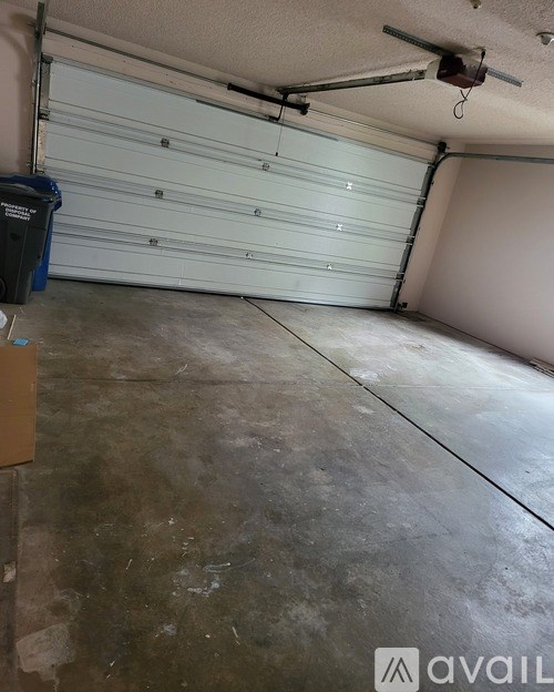 A large garage with a white roller shutter door and a blue trash bin.