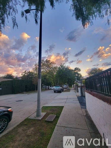 A street view with cars parked on the side and a cloudy sky.