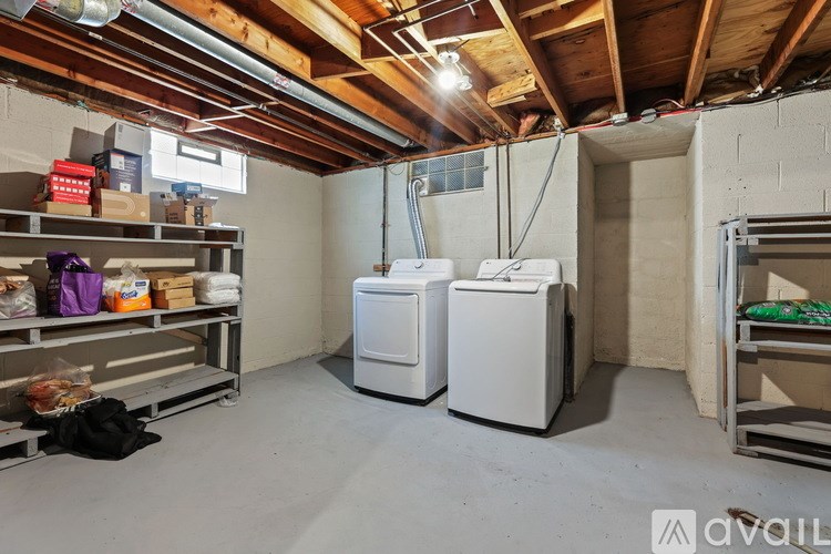A room with a white washer and dryer, a shelf with various items, and a bed with green bedding.