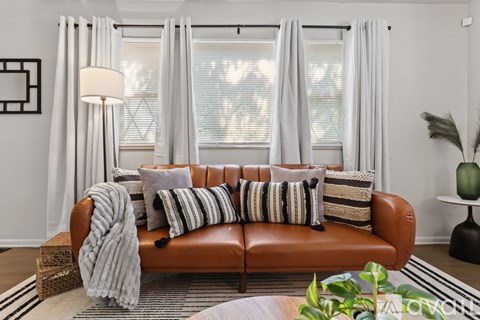 A living room with a brown leather couch and a grey throw blanket.