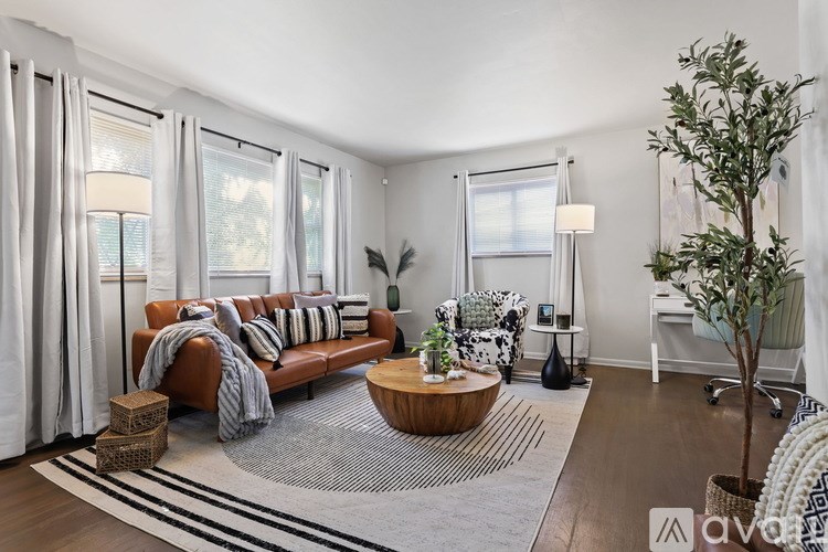 A living room with a brown leather couch, a wooden coffee table, and a large window with white curtains.