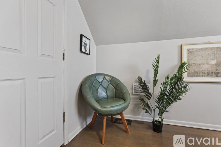 A green chair with wooden legs sits in a corner of a room with a white door and a framed picture on the wall.