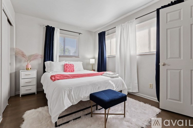 A bedroom with a white bed and a blue ottoman.