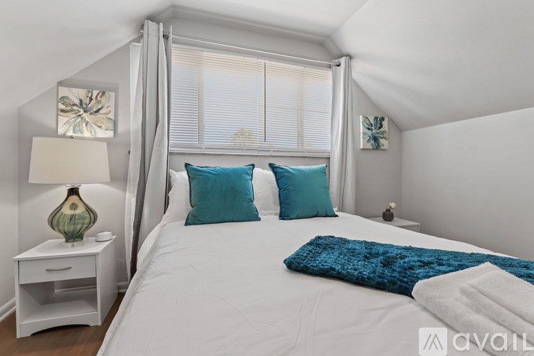 A bedroom with a white bed, blue pillows, and a white nightstand with a lamp.