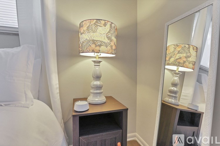 A lamp with a floral patterned shade sits on a wooden nightstand next to a bed.