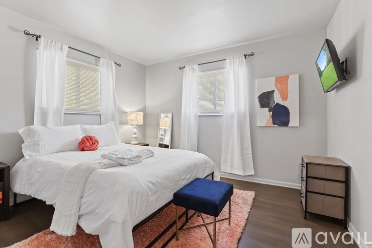 A bedroom with a white bed and a blue ottoman.