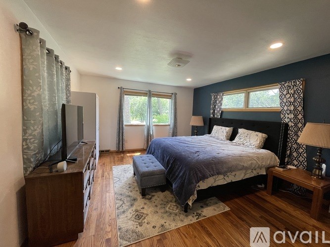 A bedroom with a bed, a television, and a window with curtains.