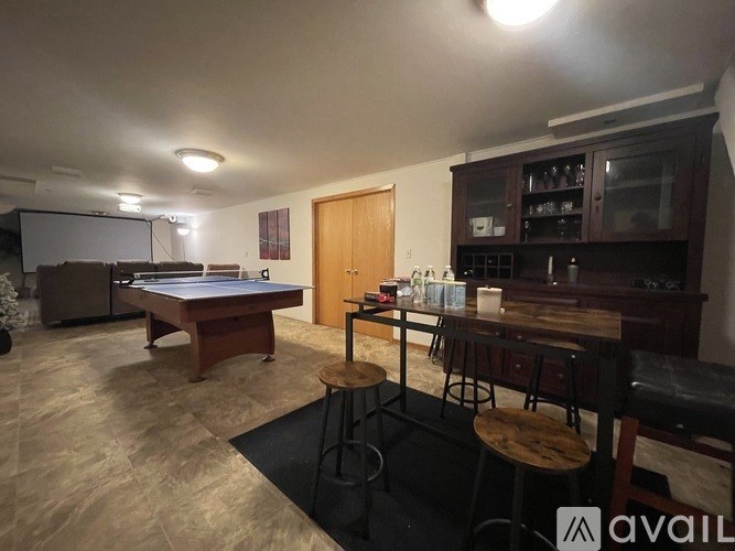 A room with a pool table, bar stools, and a cabinet with glass doors.