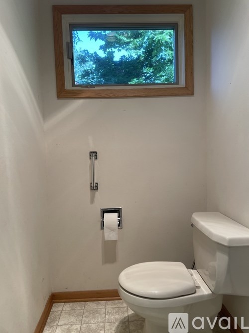 A white toilet in a bathroom with a window above it.