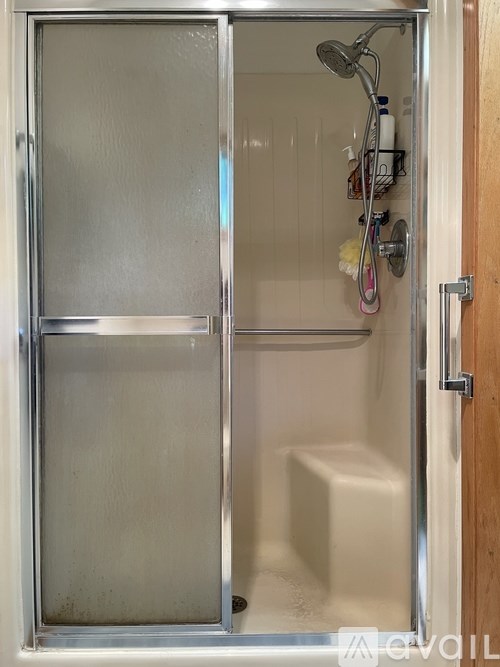 A shower stall with a glass door and a white tub.